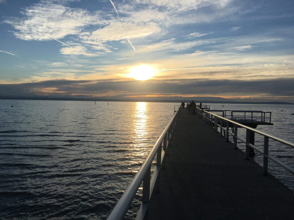 Bild von einem See im Sonnenuntergang, in den ein Steg hereinführt.