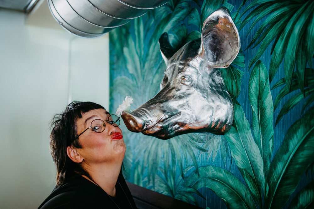 Frau küsst eine silberne Schweinsfigur vor einer grünen Wand.