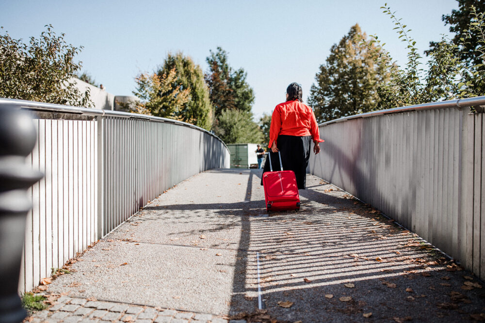 Frau mit Koffer und rotem Hemd läuft über eine Brücke.