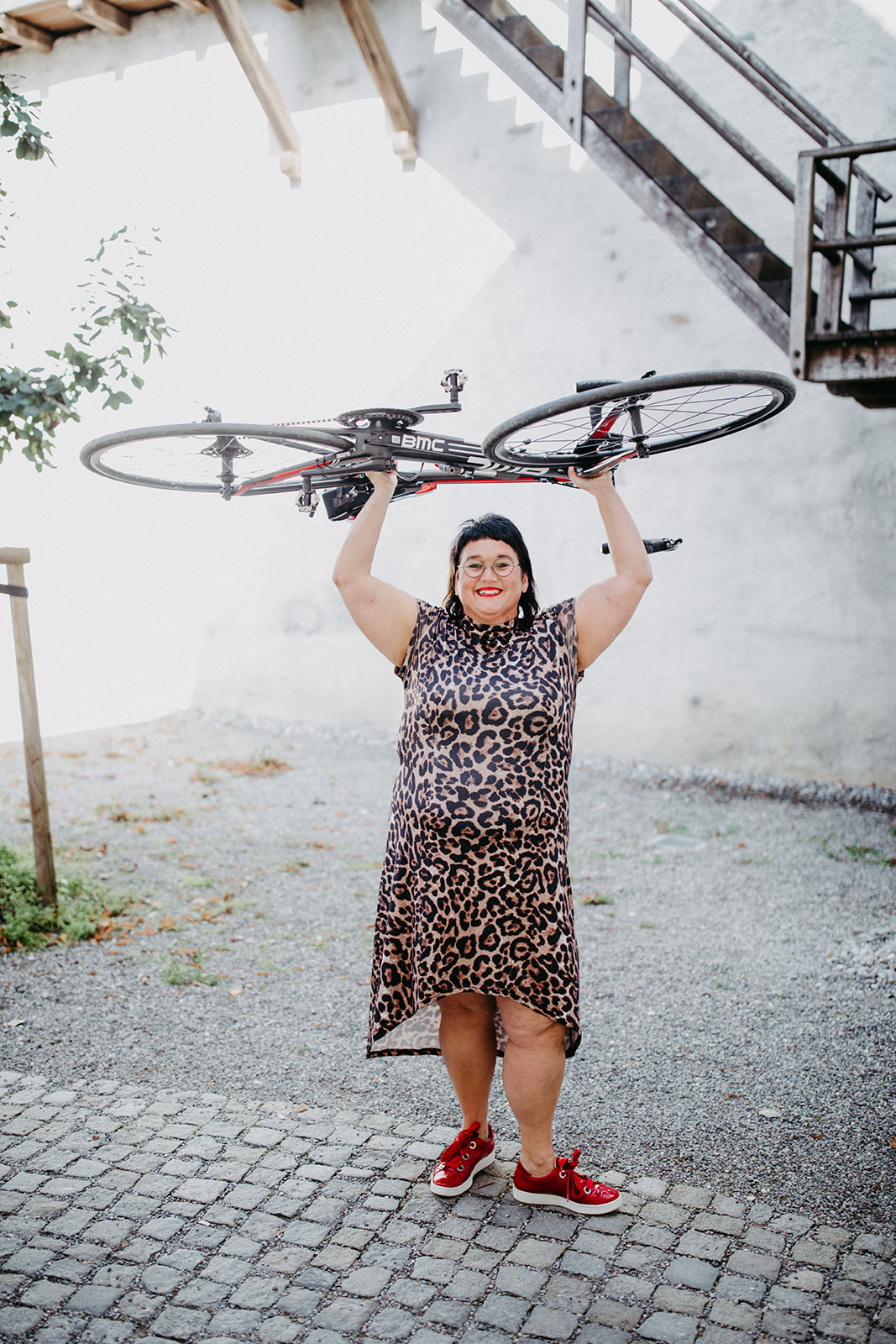 Sabine Jung-Bass hebt mit Gelassenheit ihr Rennrad in die Höhe und lächelt in die Kamera